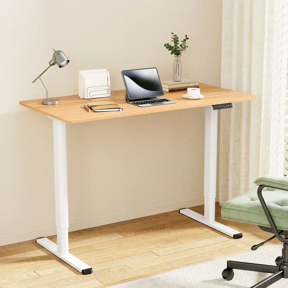 Modern adjustable standing desk with wooden top, white metal legs, laptop, lamp, notebook, and chair