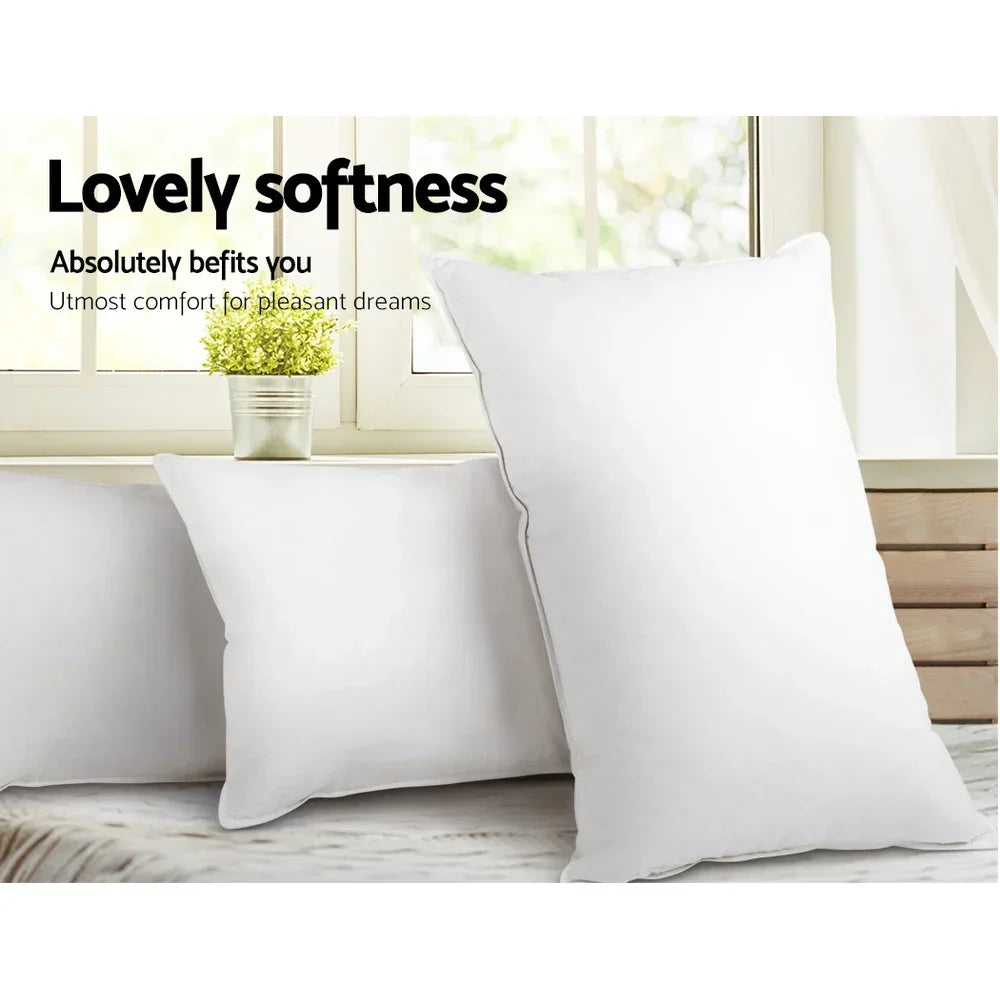 Three white soft pillows on a bed near a window with a small potted plant and curtain