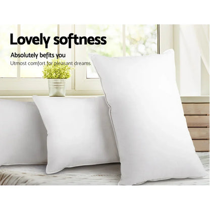 Three white soft pillows on a bed near a window with a small potted plant and curtain