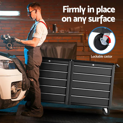 Mechanic holding engine part beside large black tool chest with lockable castor wheel in garage