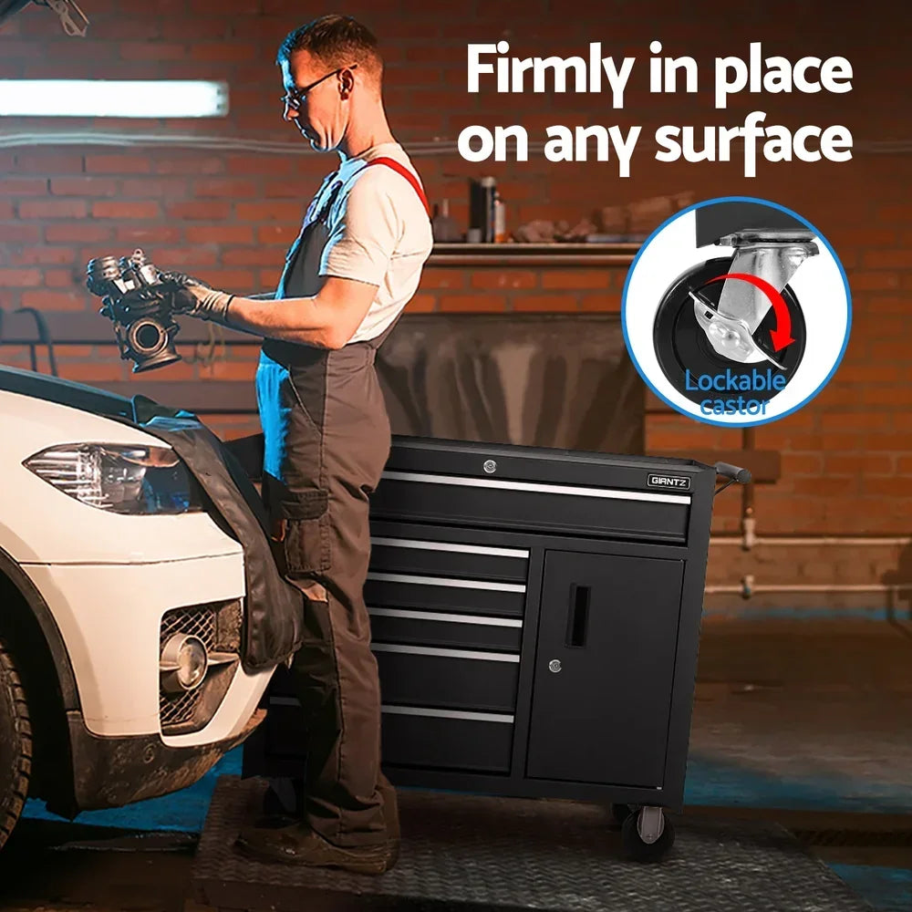 Mechanic holding car part near white SUV with black lockable caster toolbox in brick garage