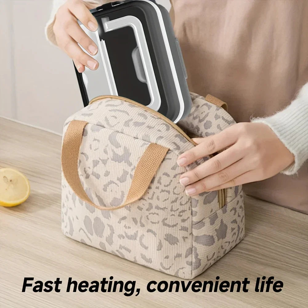 Person placing a black electric lunch box into a beige leopard print insulated bag on a kitchen counter.