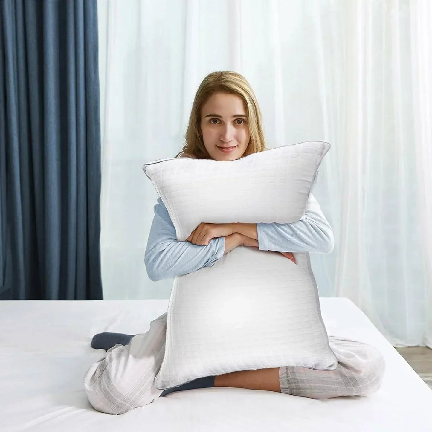 Woman sitting on bed hugging a large white textured pillow with curtains in the background