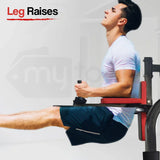 Man in gym performing leg raises on captain's chair, wearing white shirt and blue shorts