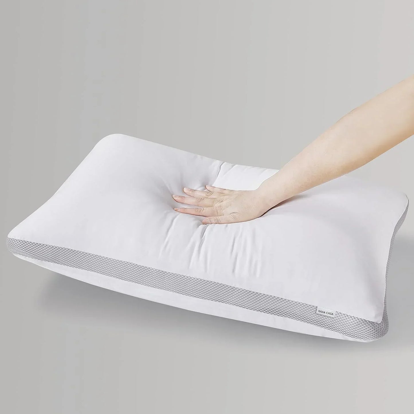 Hand pressing soft white memory foam pillow with breathable mesh sides on gray background