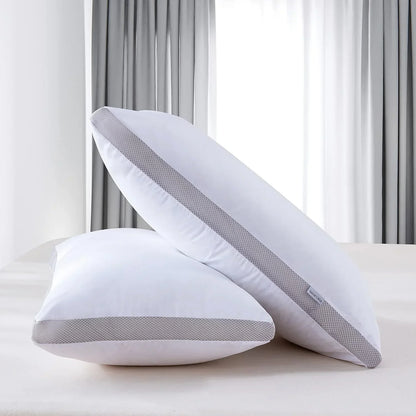 Two white pillows with gray mesh trim on a bed in a bright bedroom with gray curtains