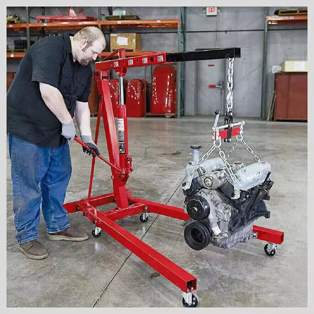 Man operating red hydraulic engine hoist lifting a car engine in a garage workshop