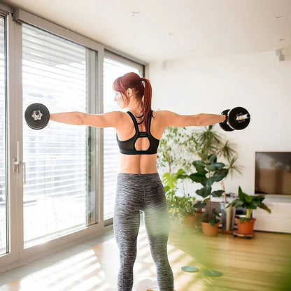 Woman in black sports bra and gray leggings lifting dumbbells in bright living room with plants and TV