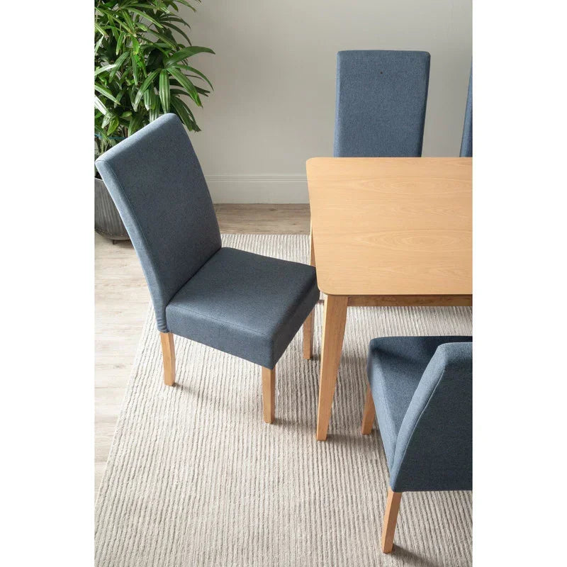 Modern dining room with light wood table, blue upholstered chairs, beige rug, and green plant