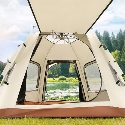 Open beige and brown camping tent set up on grassy lakeside with trees and water in background