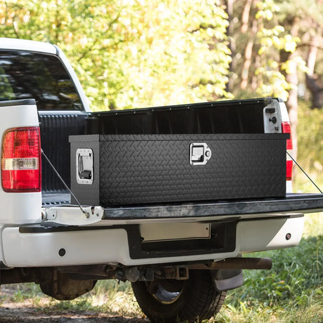 Black diamond plate pickup truck tool box on open tailgate of white truck in outdoor setting