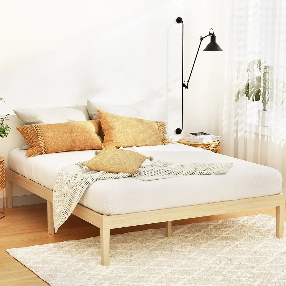 Minimalist bedroom with wooden bed frame, white bedding, tan pillows, cream throw, wall-mounted black lamp