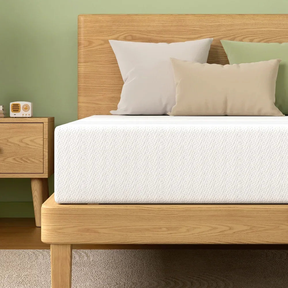 White mattress on modern wooden bed frame with green wall, pillows, and wooden nightstand